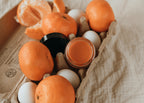 Oranges and eggs in a cardboard box on a textured surface with antioxidant balm