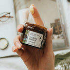 Hand holding a jar of 'Youthful Bounce' face cream with a blurred indoor background.