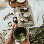 Person holding a mug with  Mira Motte nighttime skincare on a magazine on a bed