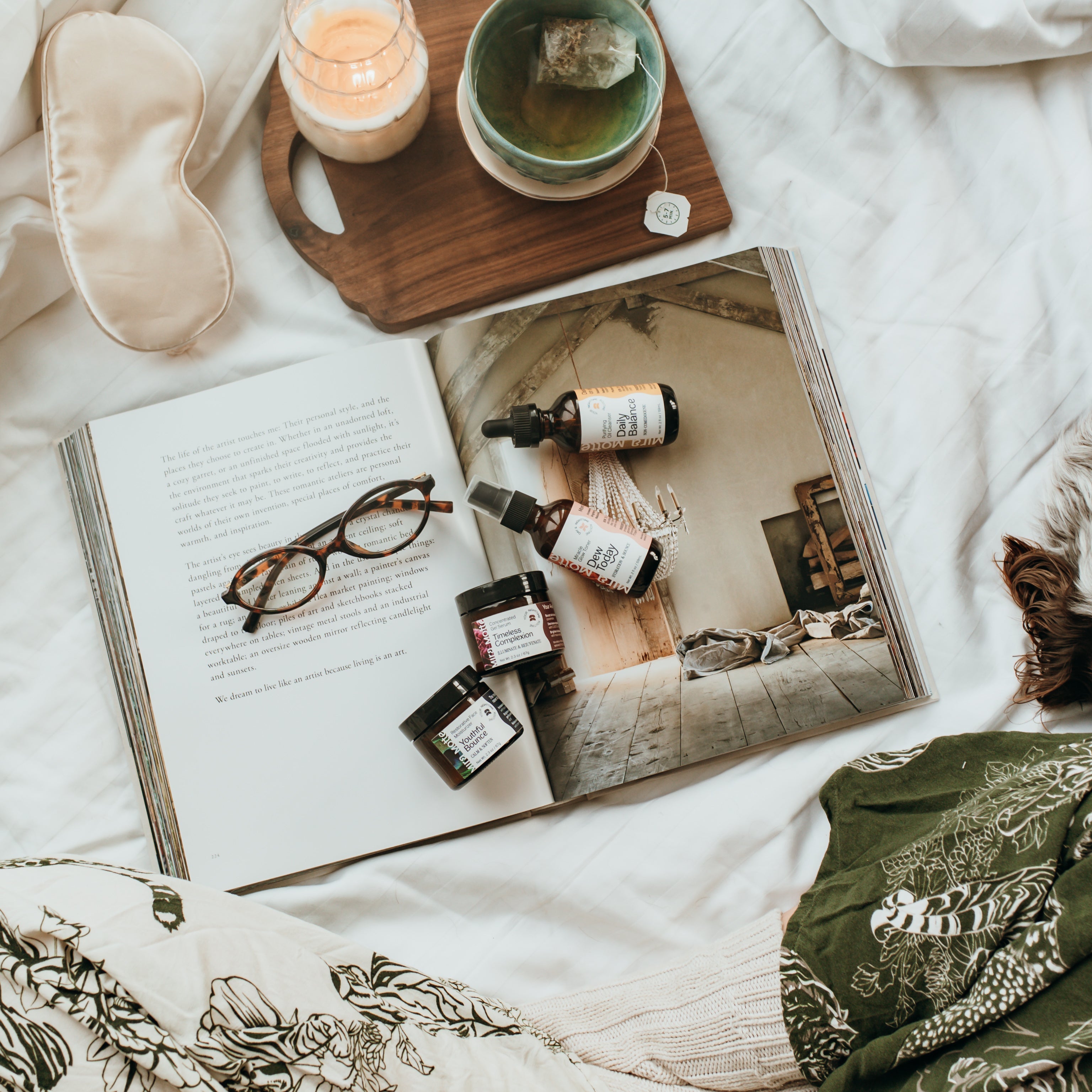 Open book with facial products, and tea on a bed