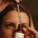 Bottle of 'Daily Balance' oil with a dropper held above a blurred face.
