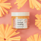 Jar of Herbal Healing balm on a pink background with yellow flowers