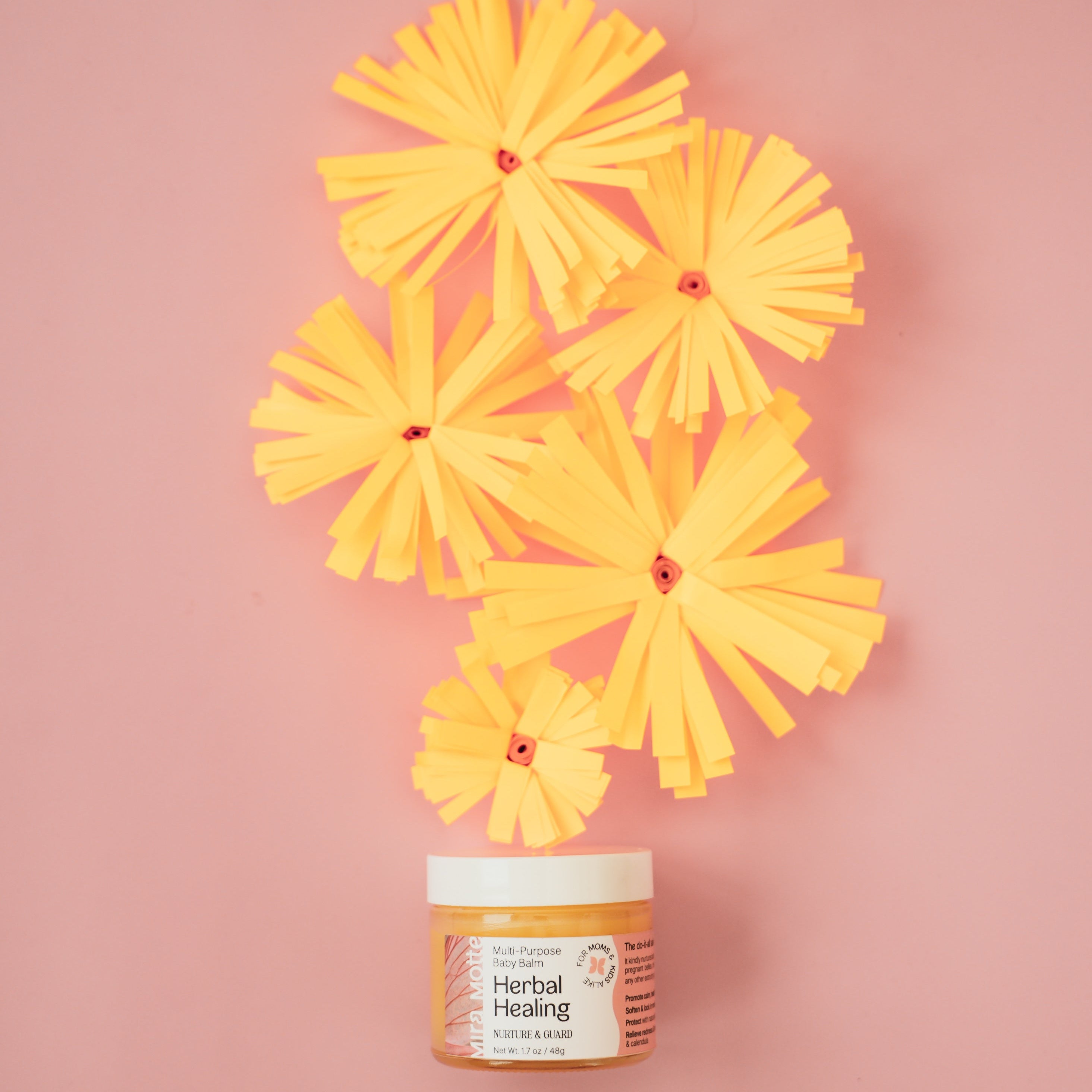 Jar of baby balm with yellow flowers on a pink background