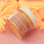 Jar of baby balm with back of the label on a pink background with yellow flowers