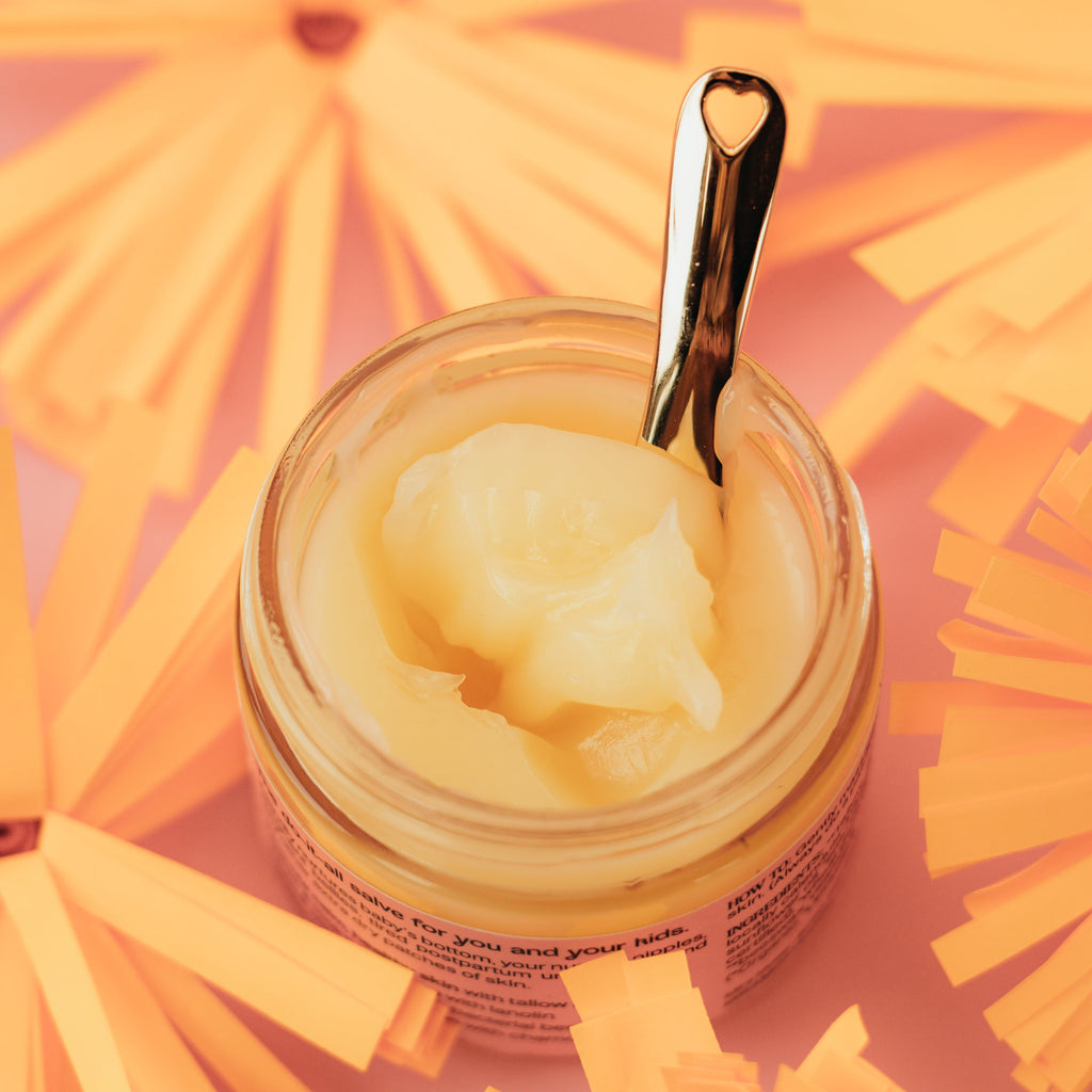 Jar of Mira Motte baby balm with a spoon on a pink background with yellow flowers
