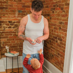 Man and child in a home setting with brick wall and wooden floor.