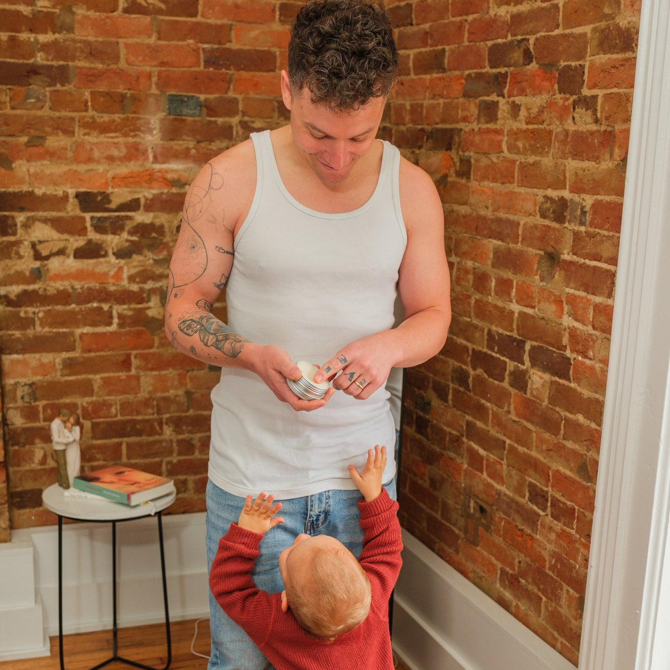 Man and child in a home setting with brick wall and wooden floor.