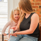 Woman and child sitting on a couch with a container of Mira Motte weightless body lotion 