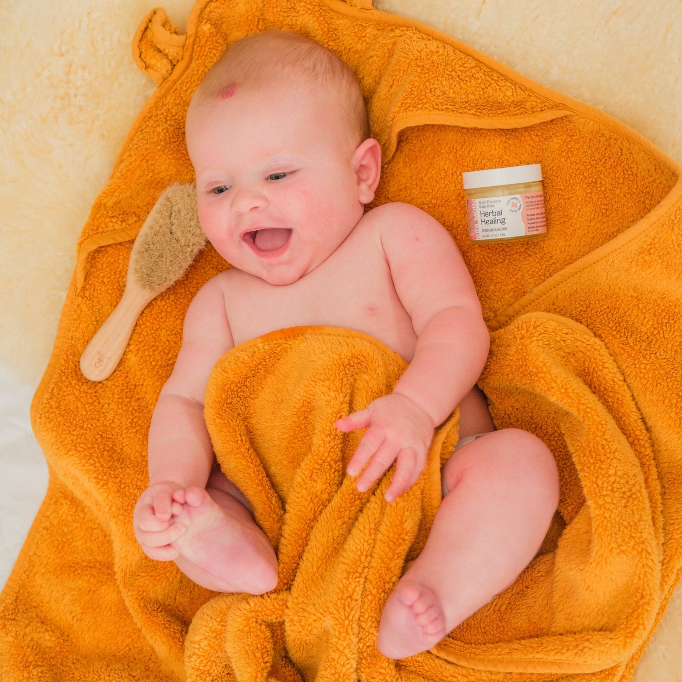Baby wrapped in an orange towel with a brush and jar of cream on a beige background