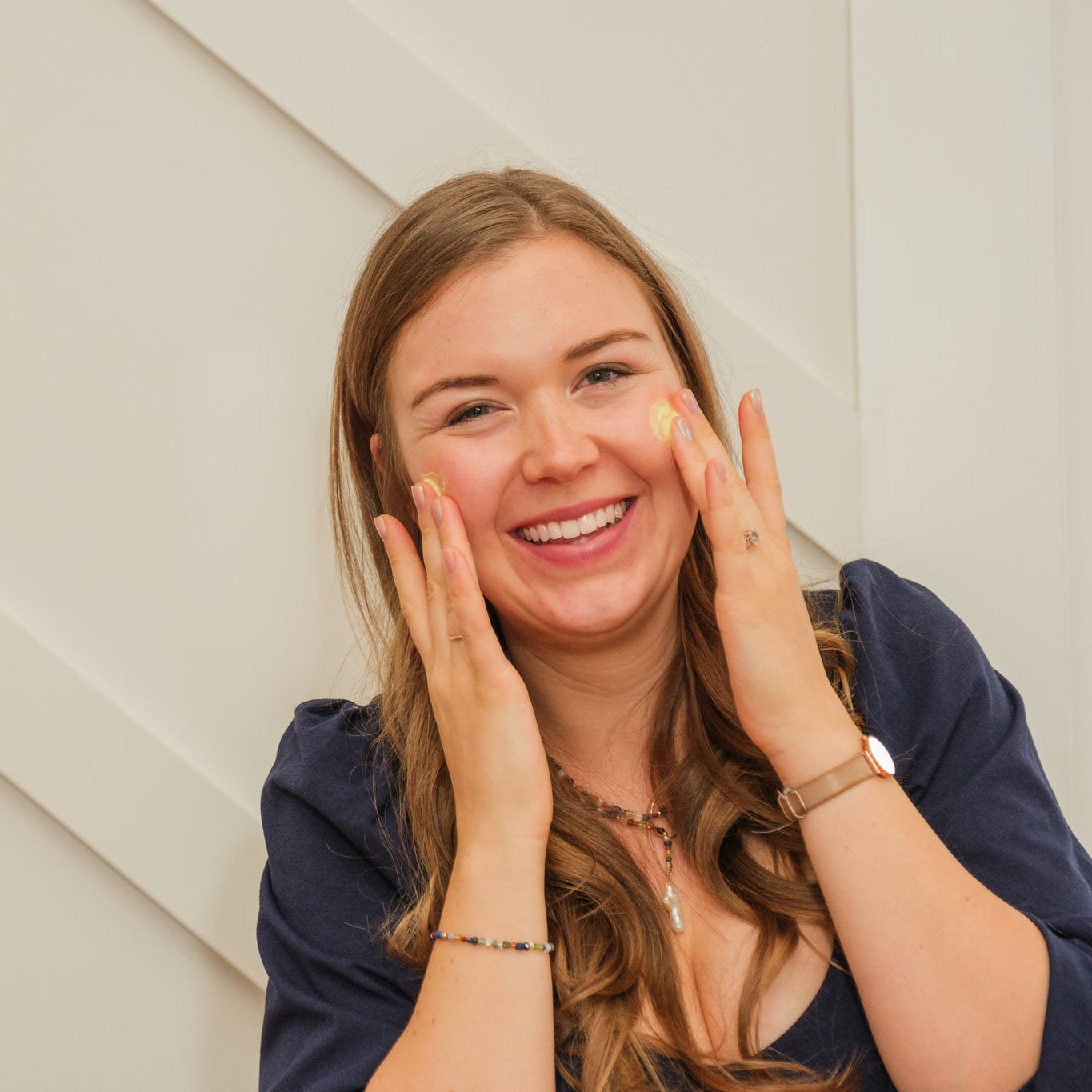 Woman applying cream to her face against a neutral background