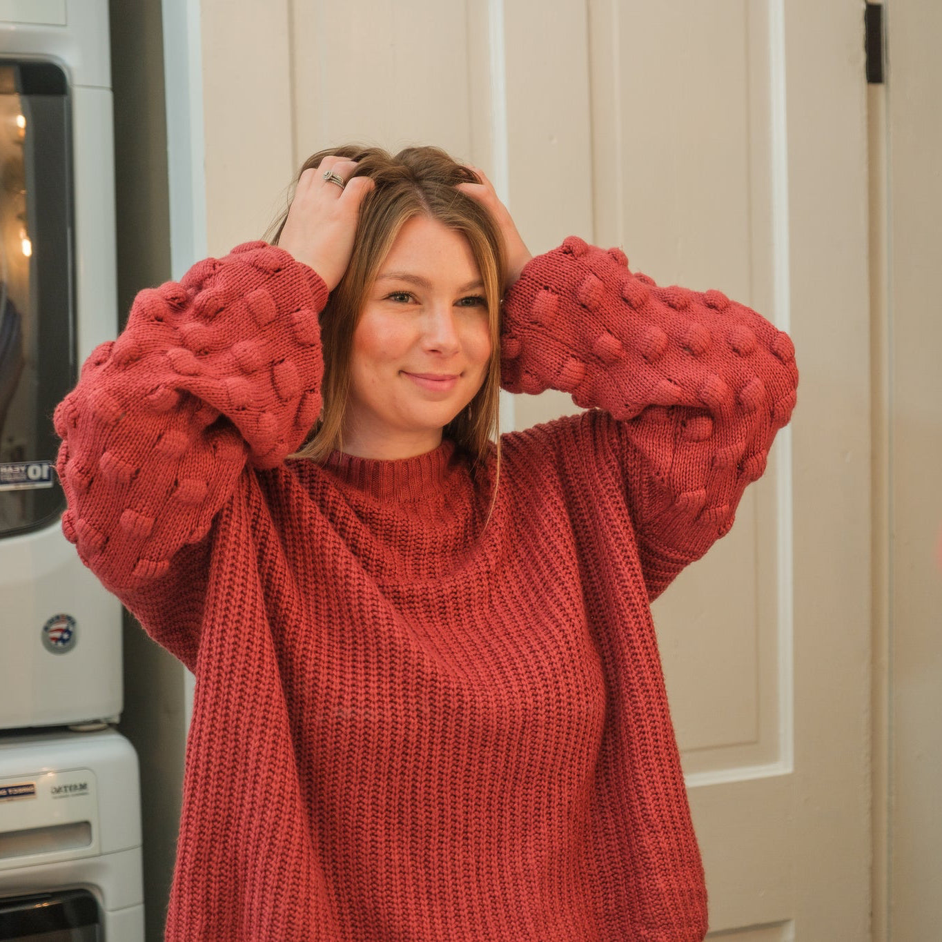 Woman wearing a red sweater adjusting her hair in front of a mirror.