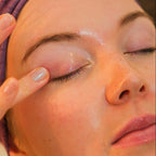 Close-up of a woman's face with a purple headband, using Mira Motte cleansing oil on her eye area.